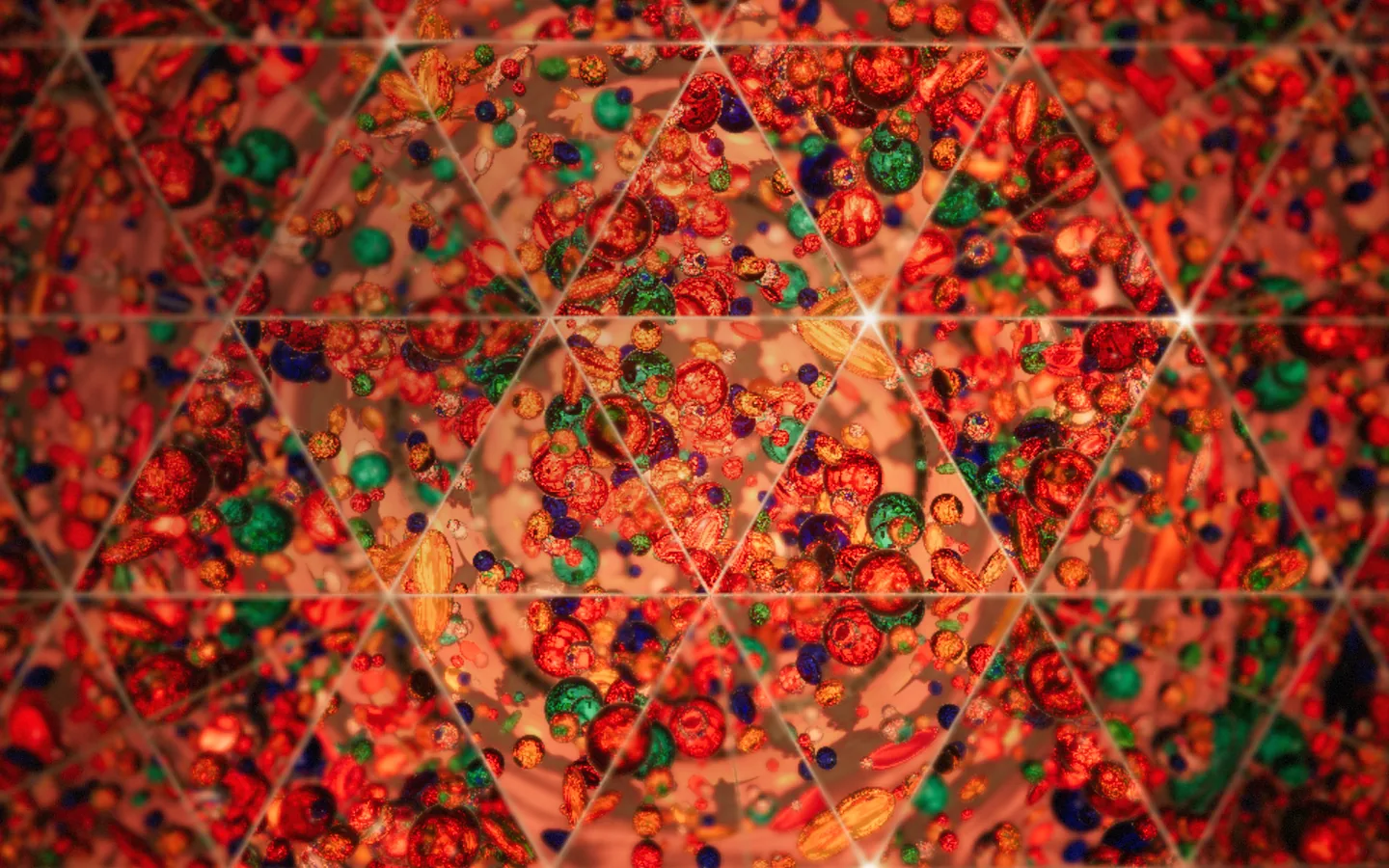 Inside the mirror tunnel: rounded pieces of red, green, blue and amber glass repeated across a triangular grid of reflections, bright seams and star glints where the mirror edges meet