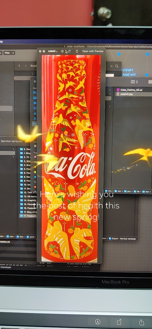 Portrait development capture showing golden birds around Coca-Cola can artwork on a laptop screen.